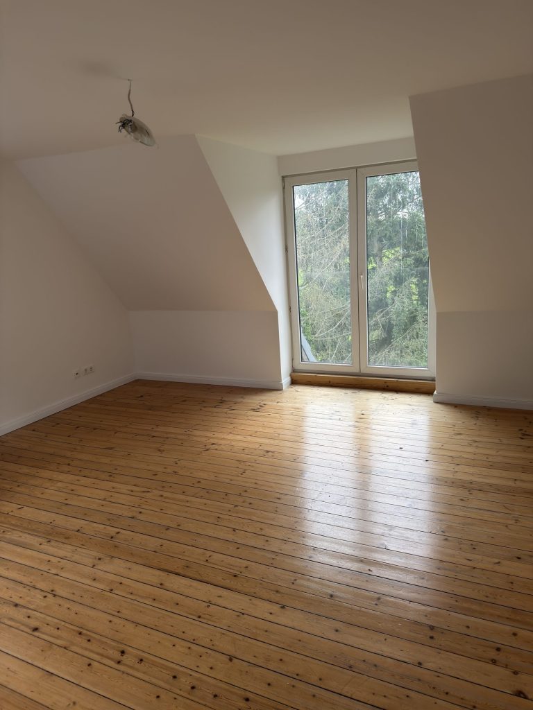 Zimmer mit Holzdielen, Dachschrägen und bodentiefem Fenster